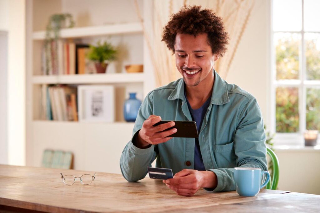 Man With Credit Card At Home Using Mobile Phone To Review Finances For Starting Business